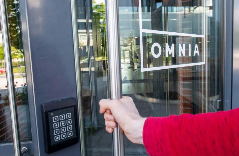 Henkilö avaa lasiovea, jossa on Omnian logo.